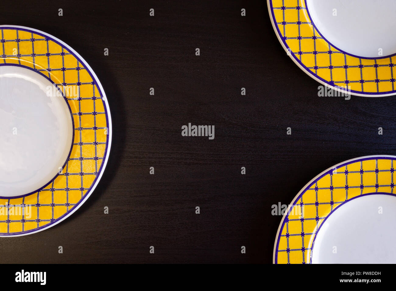 A black wooden background with three yellow and white empty plates. Stock Photo