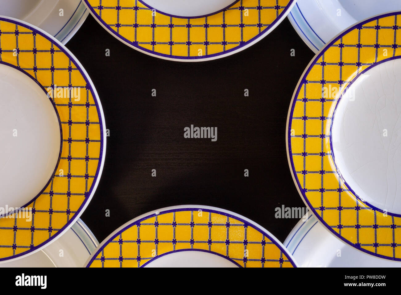 A black wooden background with four yellow and white empty plates and four blue and white empty plates. Stock Photo