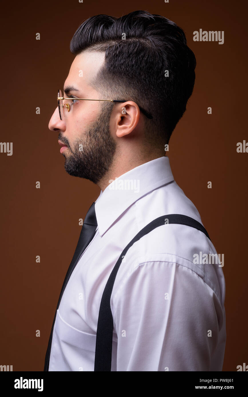 Young handsome bearded Iranian businessman against brown backgro Stock Photo