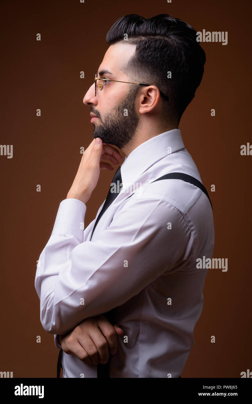 Young handsome bearded Iranian businessman against brown backgro Stock Photo