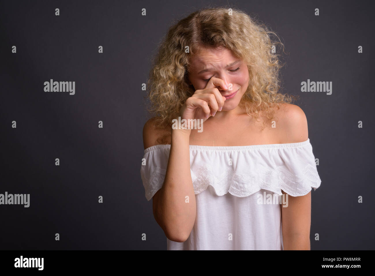 Studio shot of young beautiful woman with blond curly hair against gray background Stock Photo