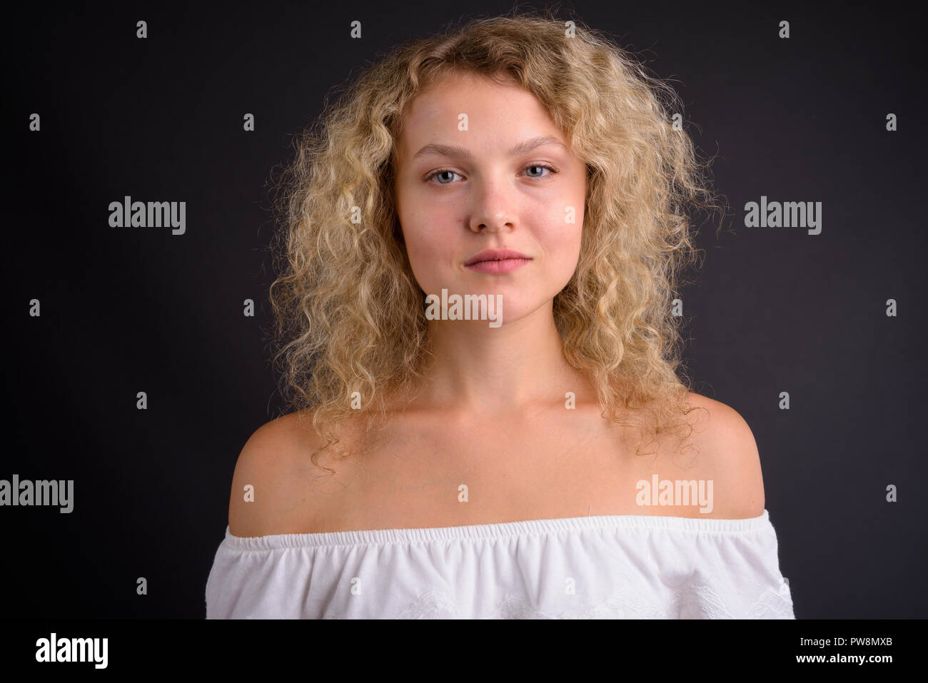 Young beautiful woman with blond curly hair against gray backgro Stock Photo