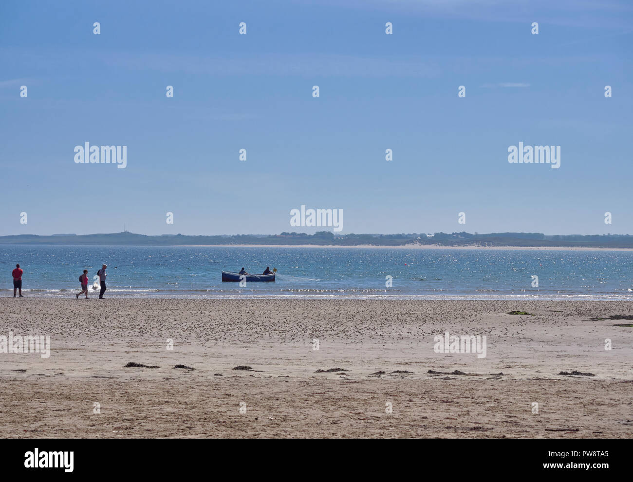 A Small Wooden Local Fishing Boat with 2 Fishermen laying its nets close to the Beach at Beadnell Bay in Northumberland, England, UK. Stock Photo
