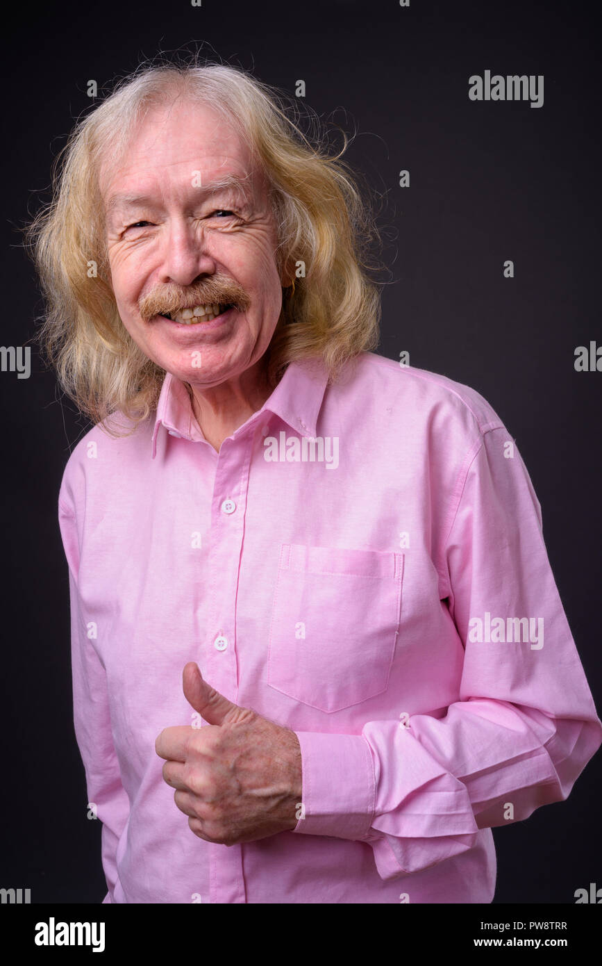 Senior businessman wearing pink shirt against gray background Stock Photo