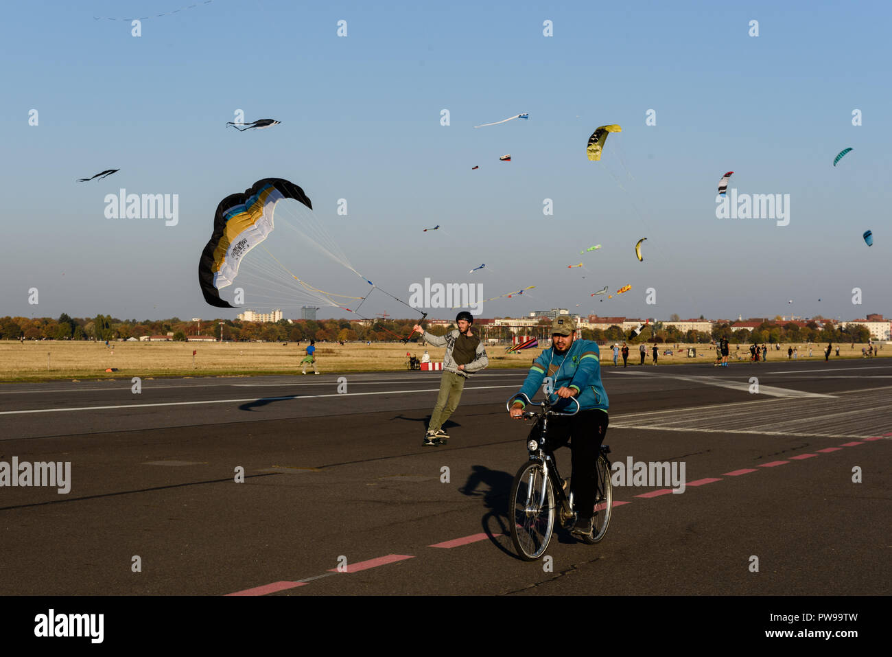 Berlin, Germany. 14th Oct, 2018. A man is seen riding a bicycle next to a man flying a kite at the Tempelhof field. The good weather in October brings many visitors to the park at the former Tempelhof Airport. Credit: Markus Heine/SOPA Images/ZUMA Wire/Alamy Live News Stock Photo