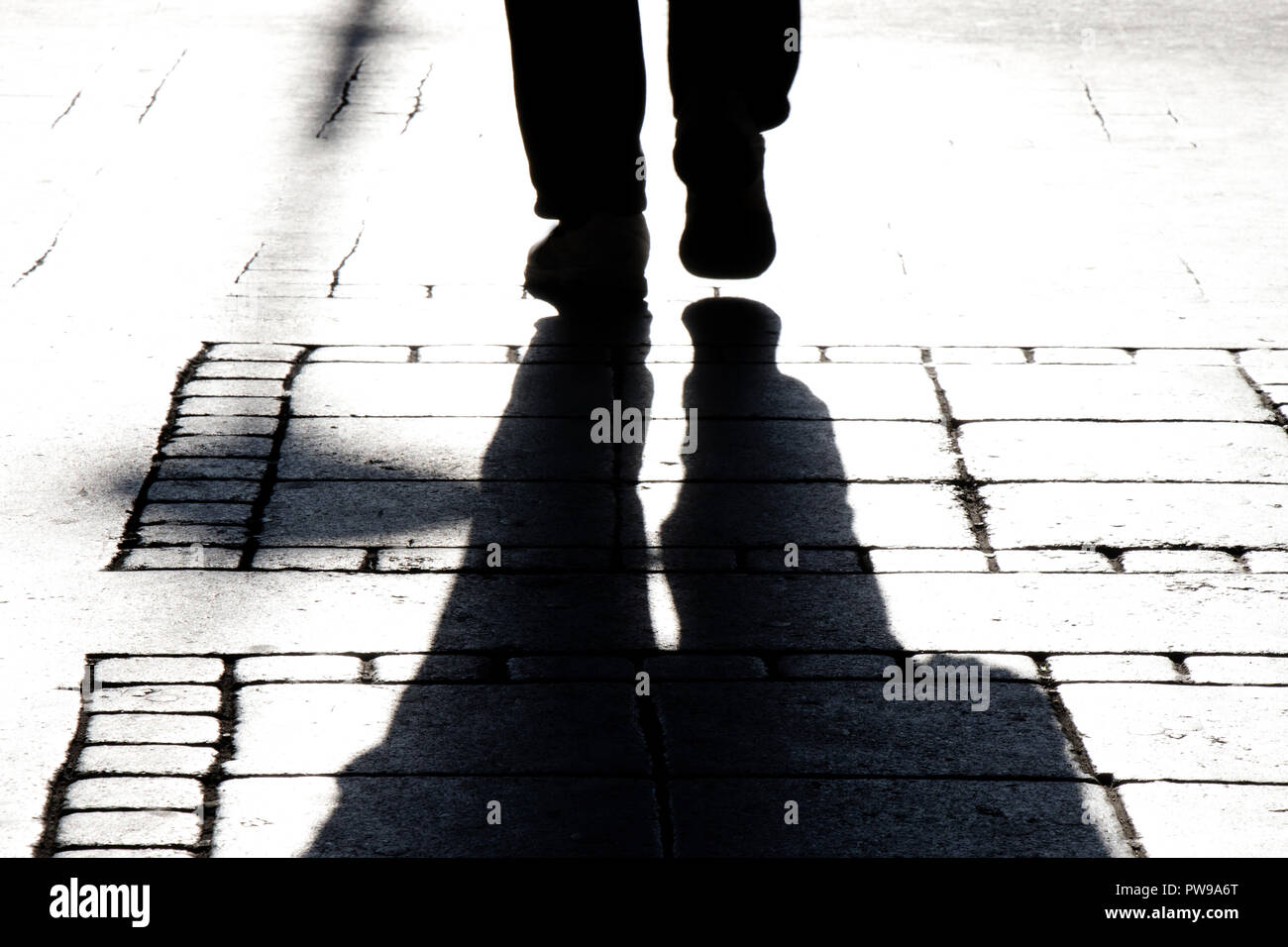 Blurry silhouette shadows of a person legs walking on city street sidewalk in black and white Stock Photo