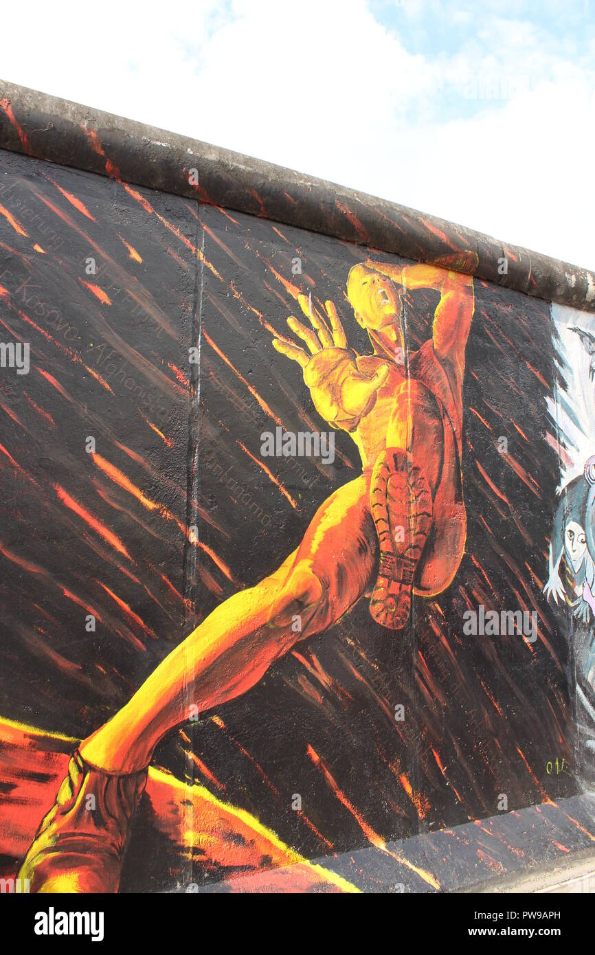 East Side Gallery, Berlin Wall - Welcome (Willkommen), Oliver Meline (Feind) painting of golden man in pain surrounded by fire Stock Photo