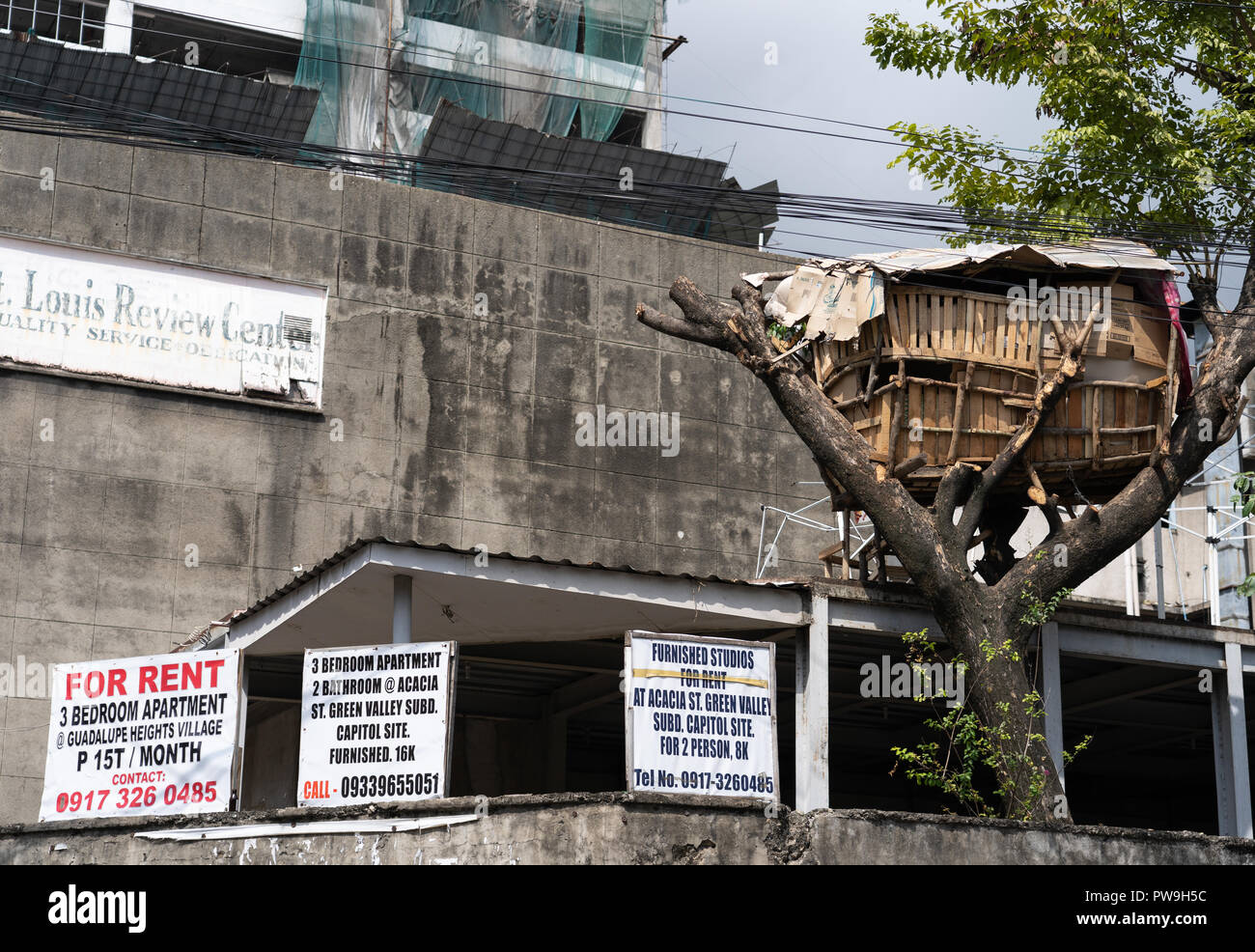 Juxtaposition image with a sign on a hoarding and a tree house alongside. Stock Photo
