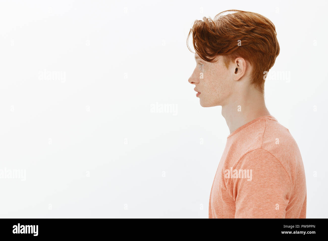 Profile shot of stylish and confident redhead young male with freckles posing for portfolio with serious cool expression, being calm while posing over gray wall, dreaming become famous model Stock Photo