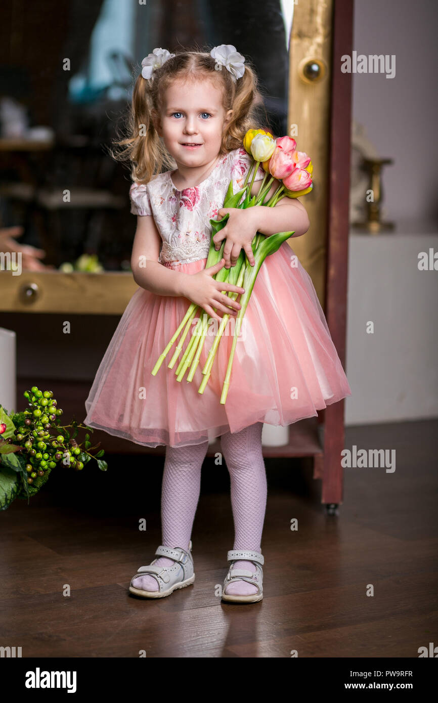 blue-eyed cute girl in a pink dress holding in her hands an armful of tulips Stock Photo