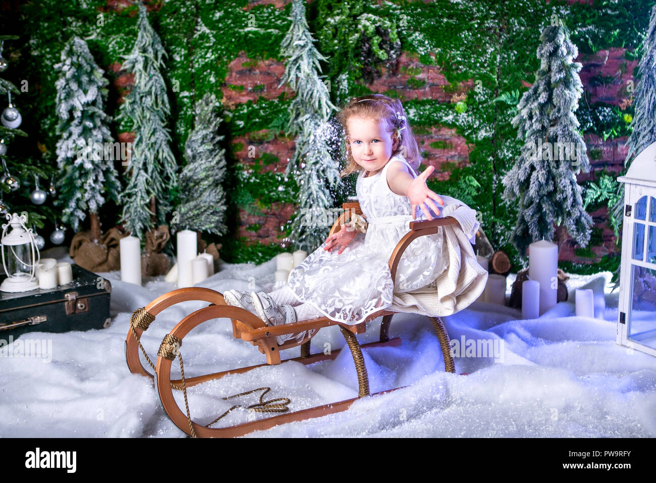 cute little princess in a white dress is sitting on a sled and throwing snow Stock Photo