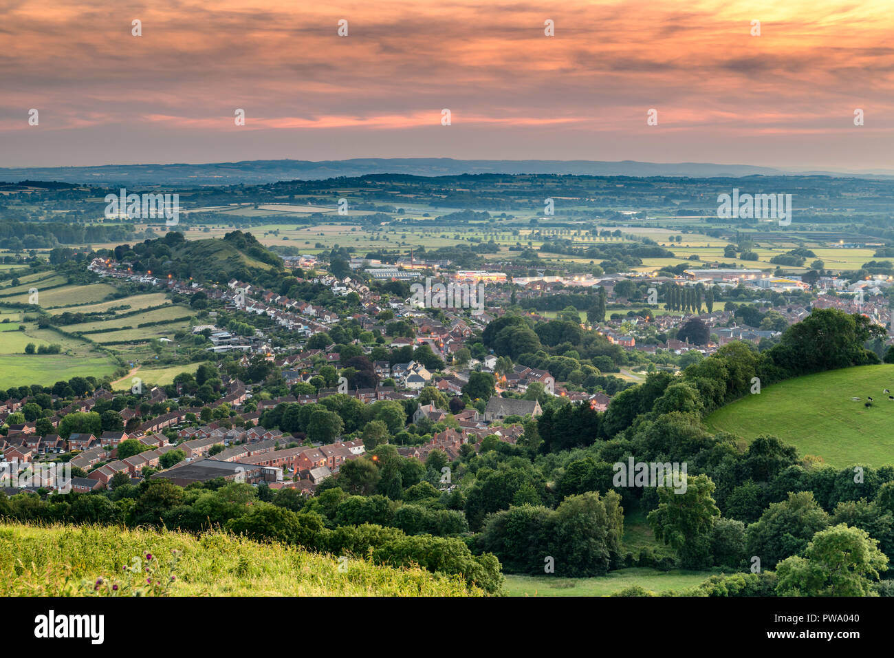 The lights slowly come on in the town of Glastonbury as the sun sets over the Somerset  Levels. Stock Photo