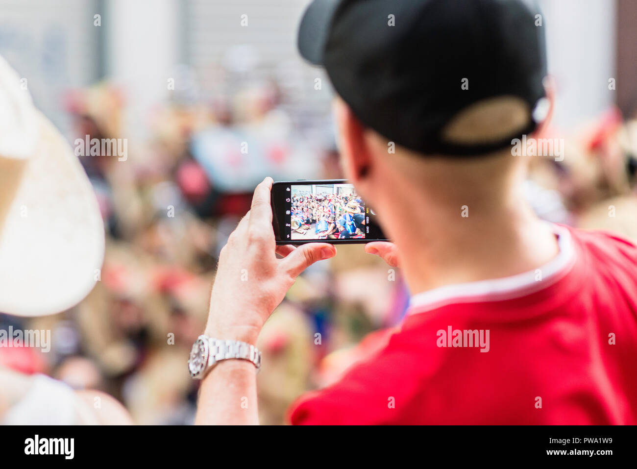 Man wearing a hat taking photographs with his smart phone during the Festa Major. Summer 2018 Stock Photo