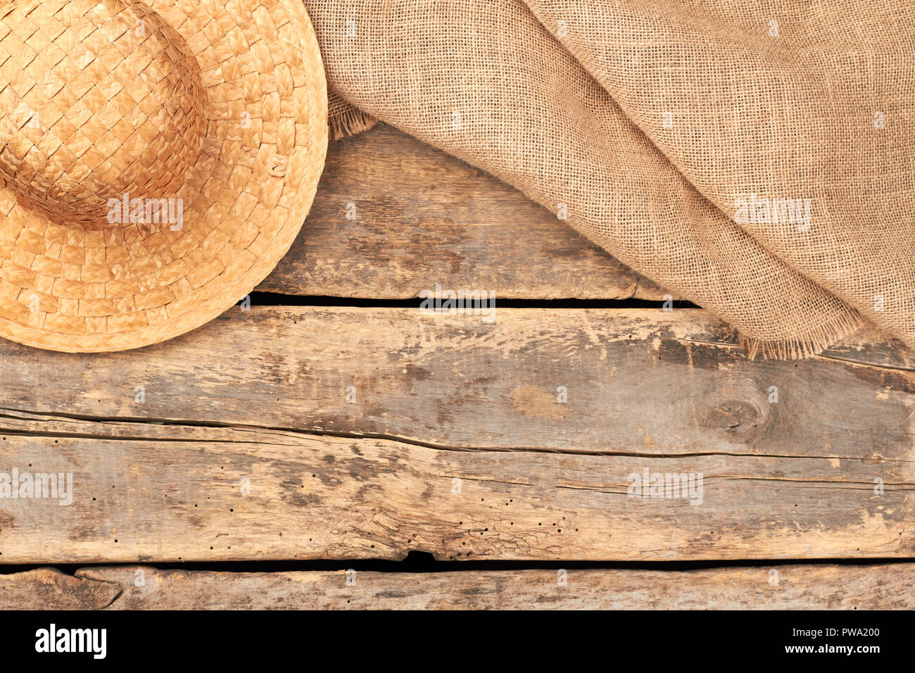 Burlap hessian sacking and straw hat. Flat lay background with straw hat and burlap fabric on rustic wooden floor. Vintage style. Stock Photo