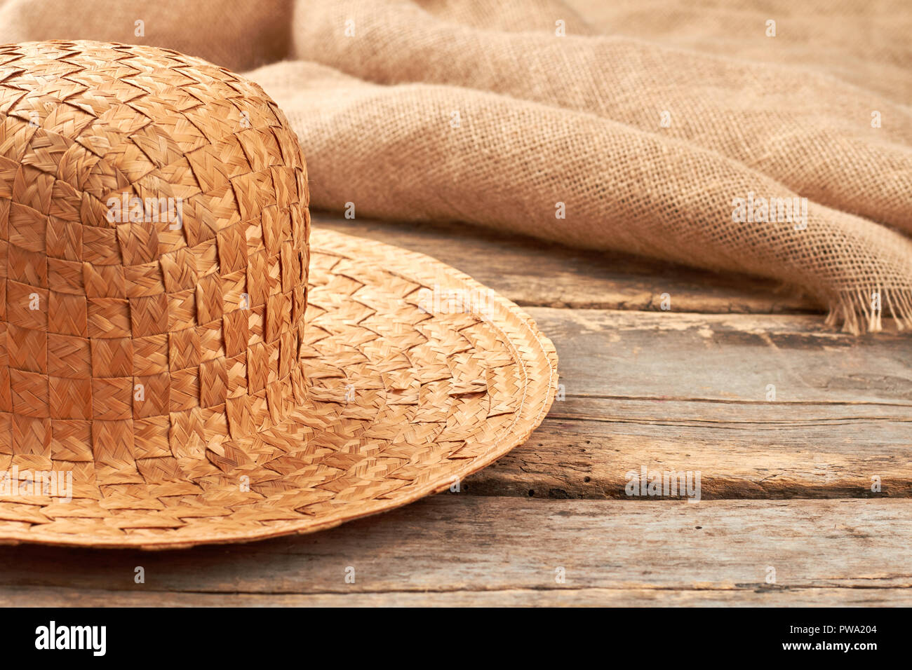 Straw hat on rustic wooden background. Natural wicker hat and hessian fabric cloth on wooden planks. Stock Photo