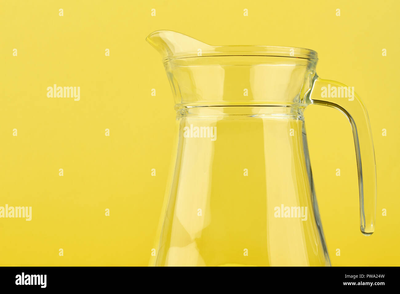Clean glass jug on yellow background. Blank transparent pitcher on