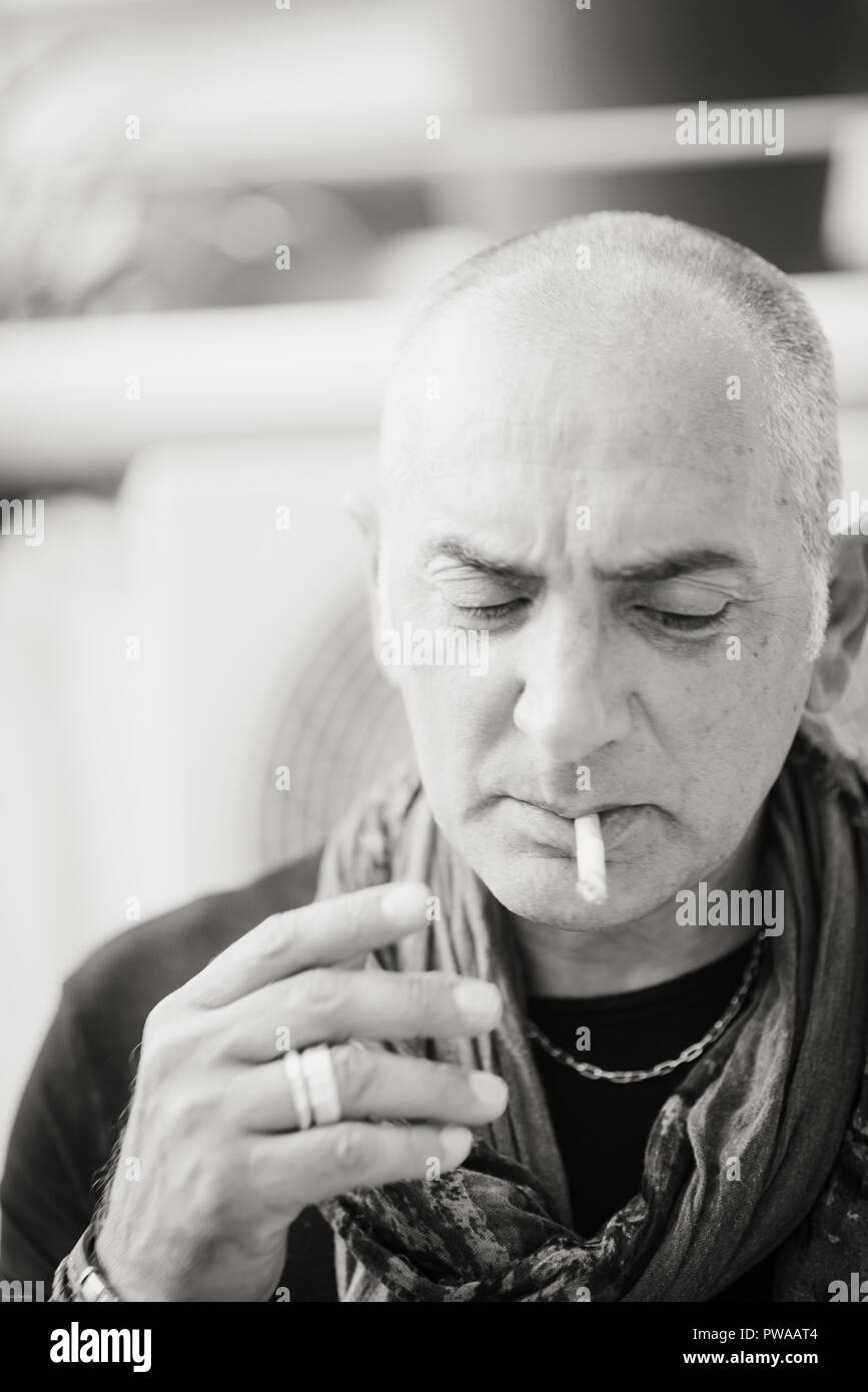 A 50y man is smoking a cigarette. Black and white. The fan coil of an