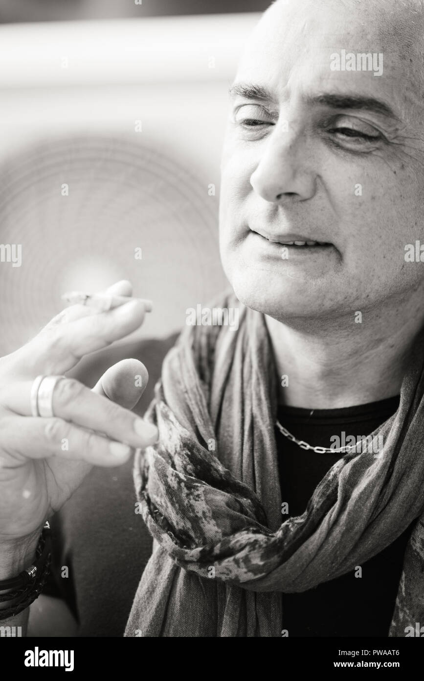 A 50y man is smoking a cigarette. Black and white. The fan coil of an