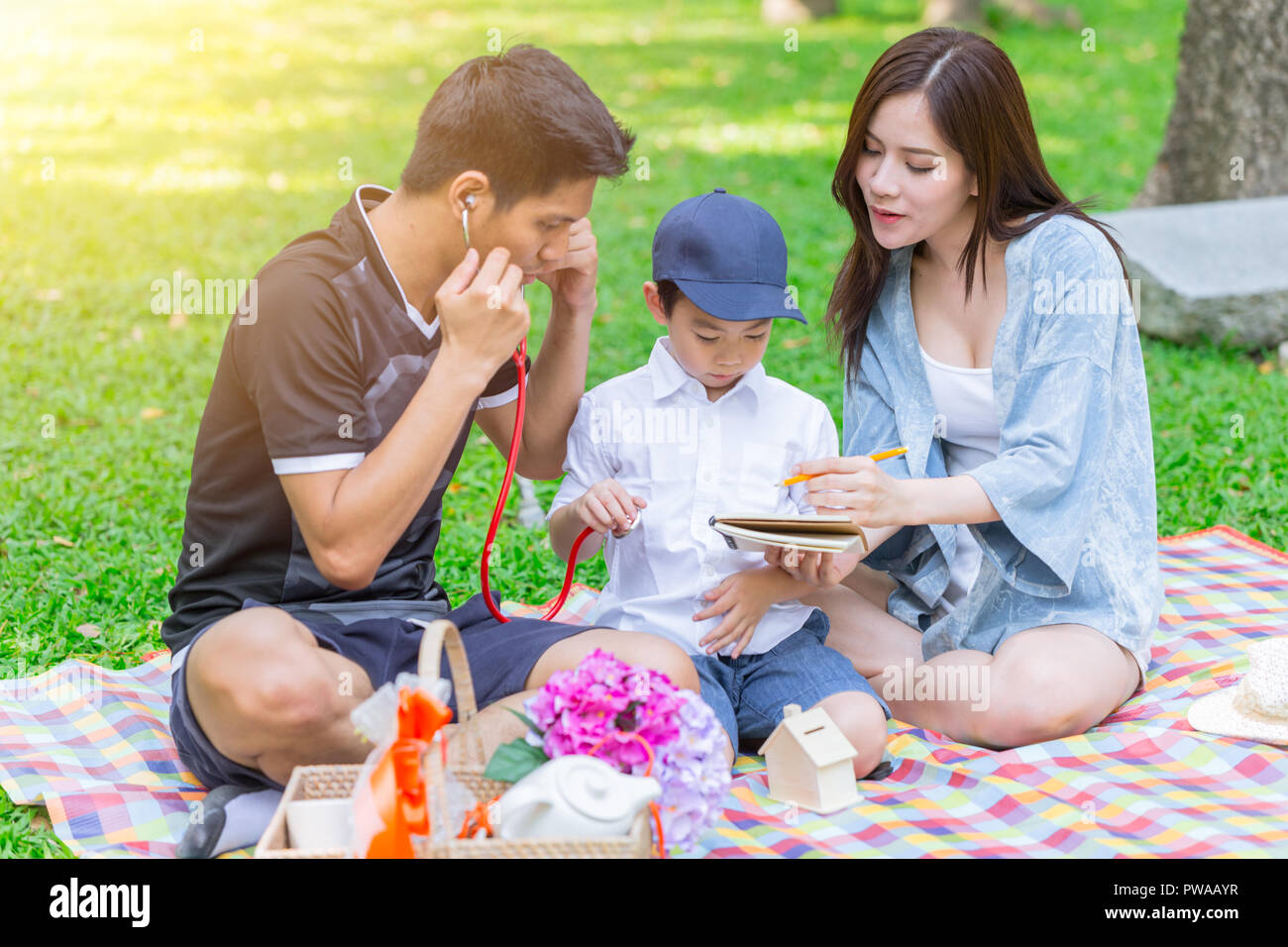 Asian teen family teaching son homework while picnic at outdoor park Stock Photo