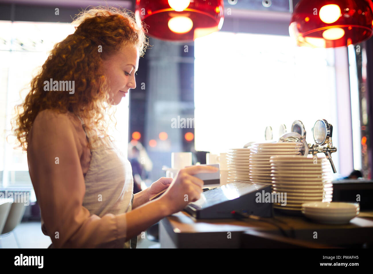 Young waitress standing by counter and using electronic cashbox while entering payment bill information Stock Photo