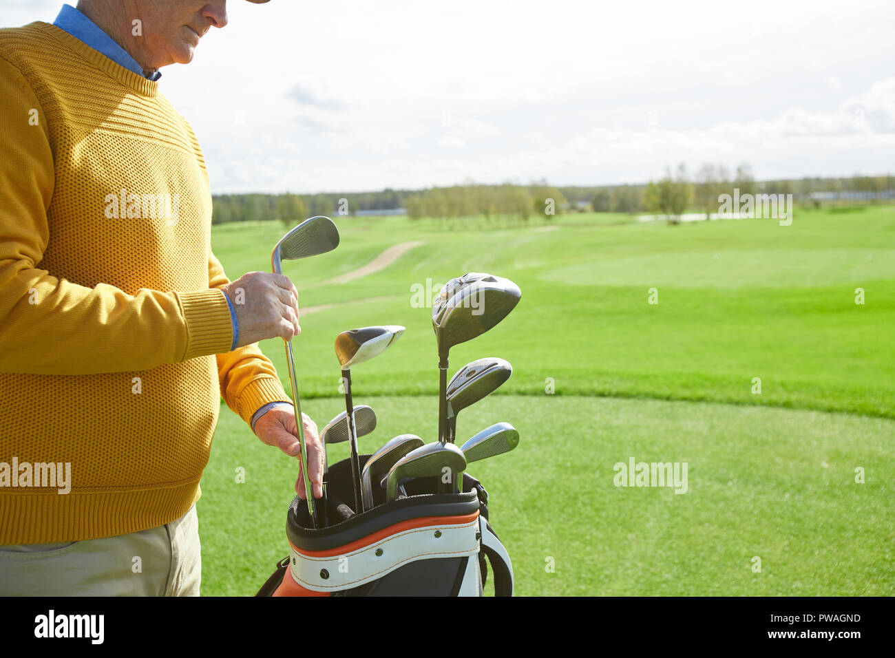 Senior professional golf player taking out one of clubs off bag before