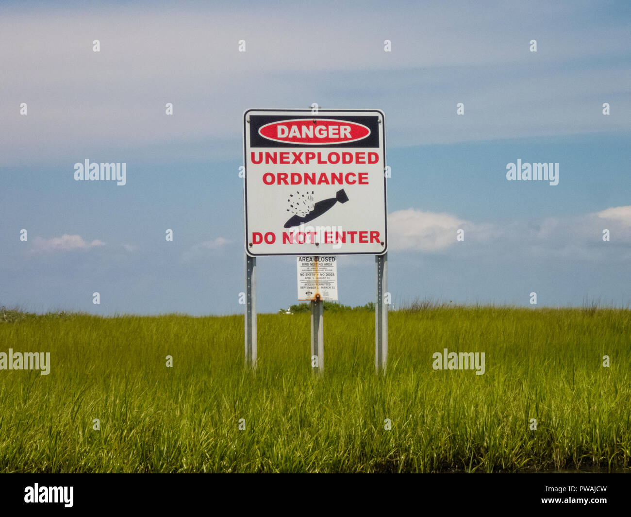 Danger unexploded ordnance do not enter  posted sign above green sea grass in front of a blue sky wide view Stock Photo