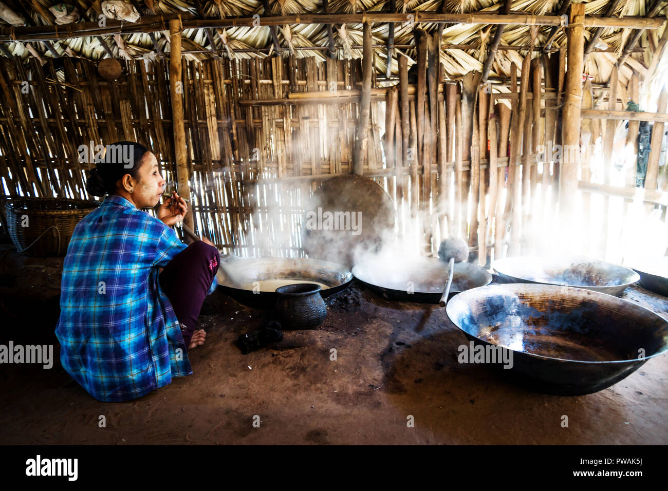 Burmese woman smoking cigar and cooking palm sugar in a hut near Bagan