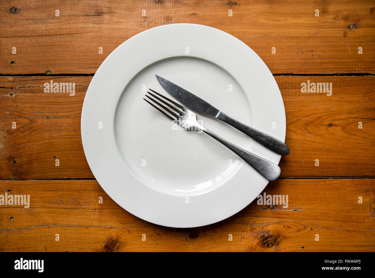 Top view of silver fork and knife on round white plate on wooden table reffering that dinner is finished Stock Photo