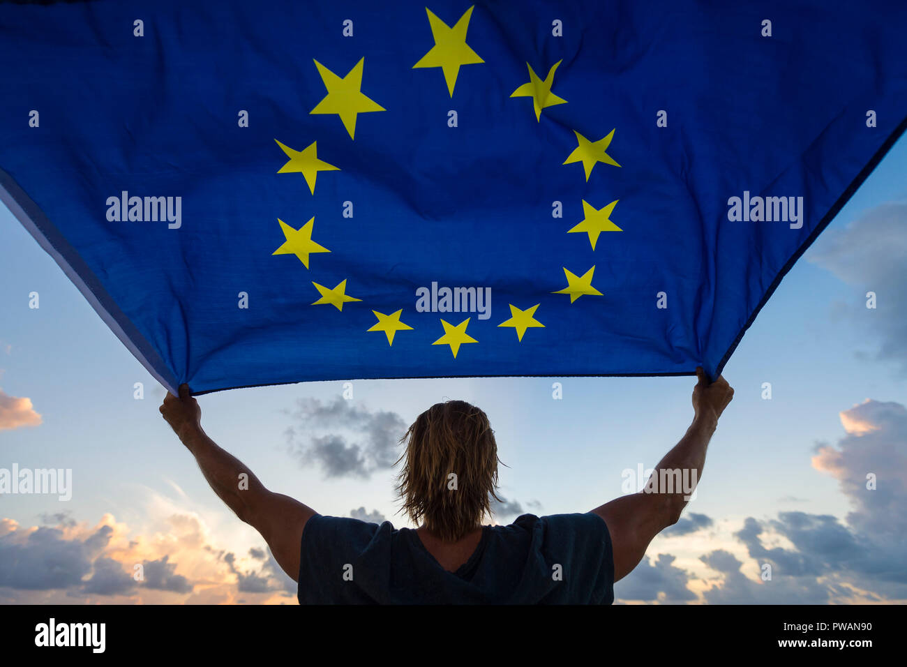 Silhouette of person holding European Union flag against soft sunset sky Stock Photo