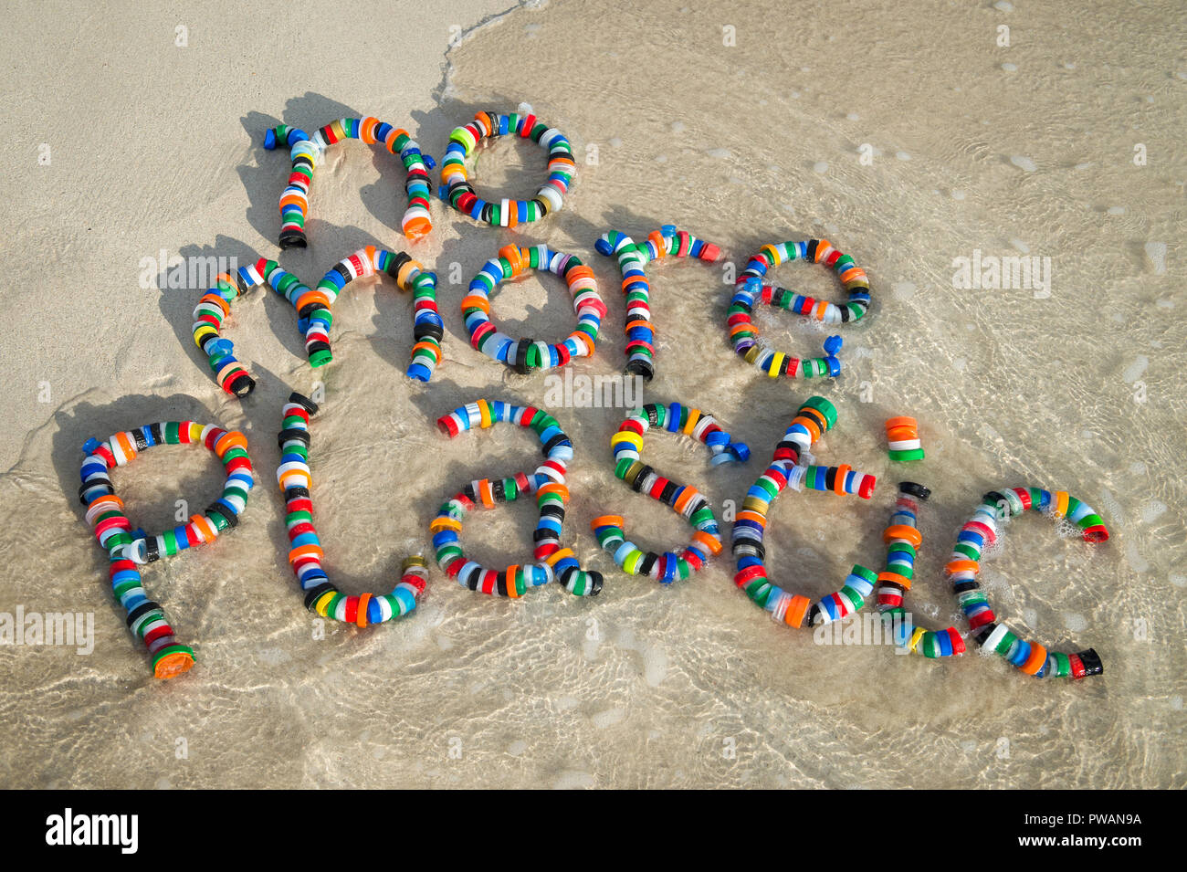No More Plastic message made from colorful used bottle cap garbage on the smooth sand shore of a tropical beach Stock Photo