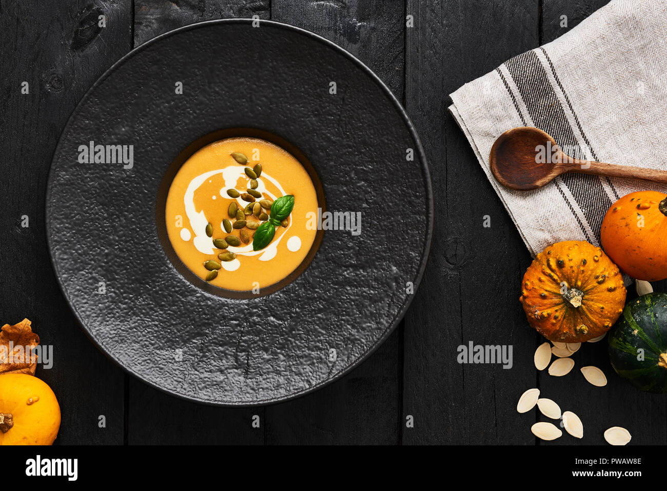 Pumpkin and carrot soup with pumpkin seeds, cream and basil in black modern plate on dark wooden background. Top view. Stock Photo