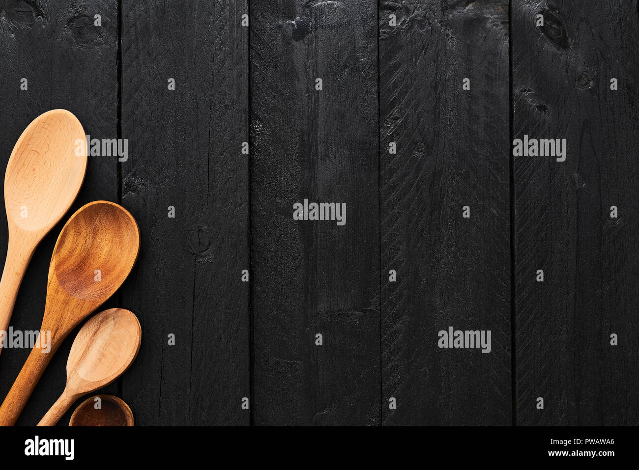 Wooden spoons on black wooden background with copy space. A collection of wooden kitchen utensils on dark wooden background. Top view. Stock Photo