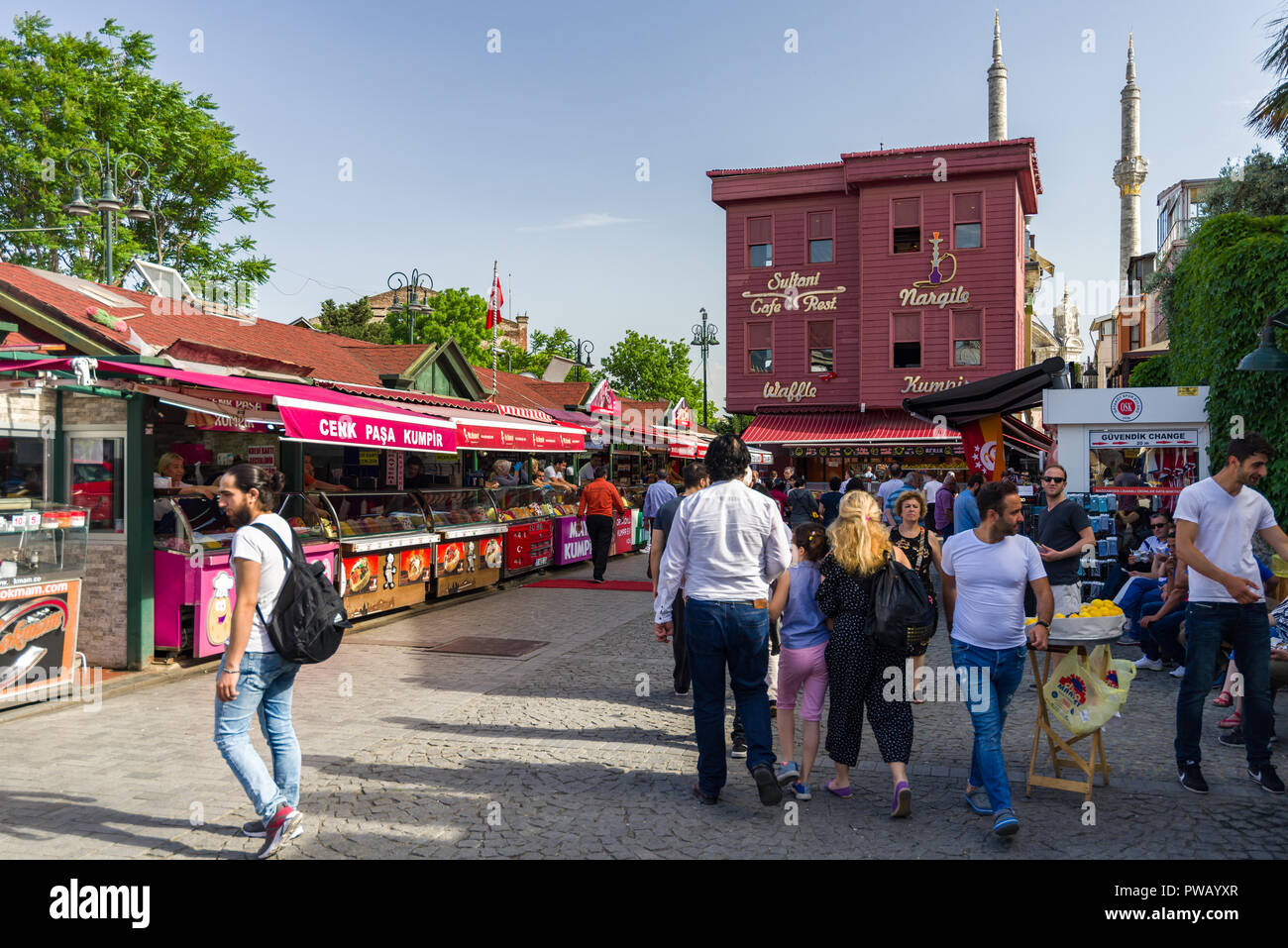 Various stalls selling Kumpir or baked potatoes line a cobbled street as people walk past in the Ortaköy district, Istanbul, Turkey Stock Photo