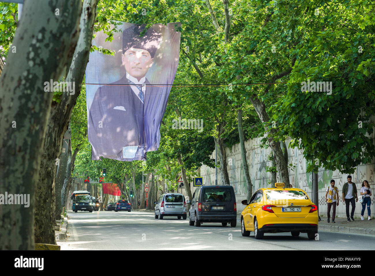 A large flag with Mustafa Kemal Atatürk printed on it waves above a tree lined avenue with vehicles driving on it, Istanbul, Turkey Stock Photo