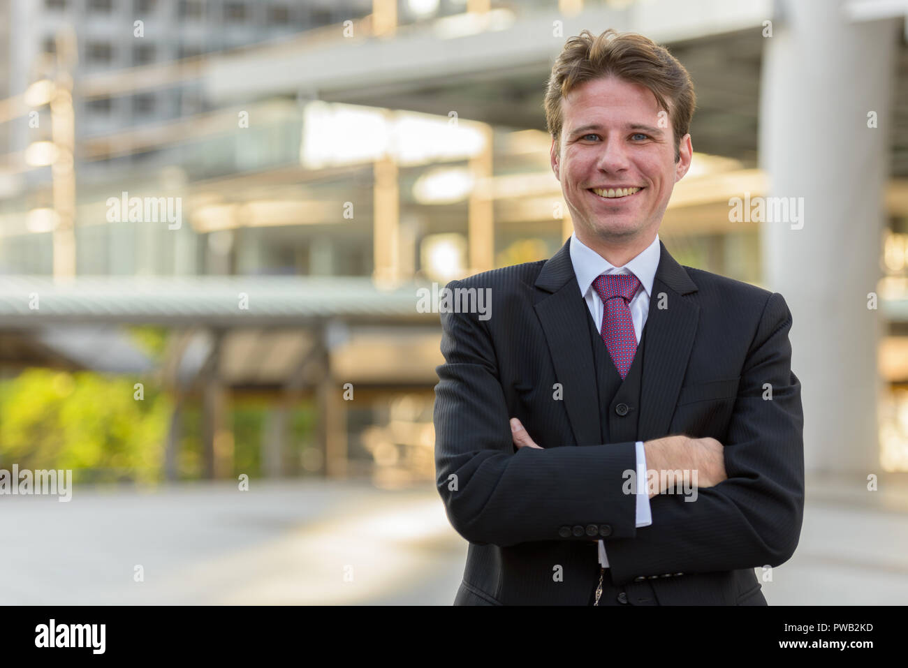 Happy businessman smiling with arms crossed in front of modern b Stock ...