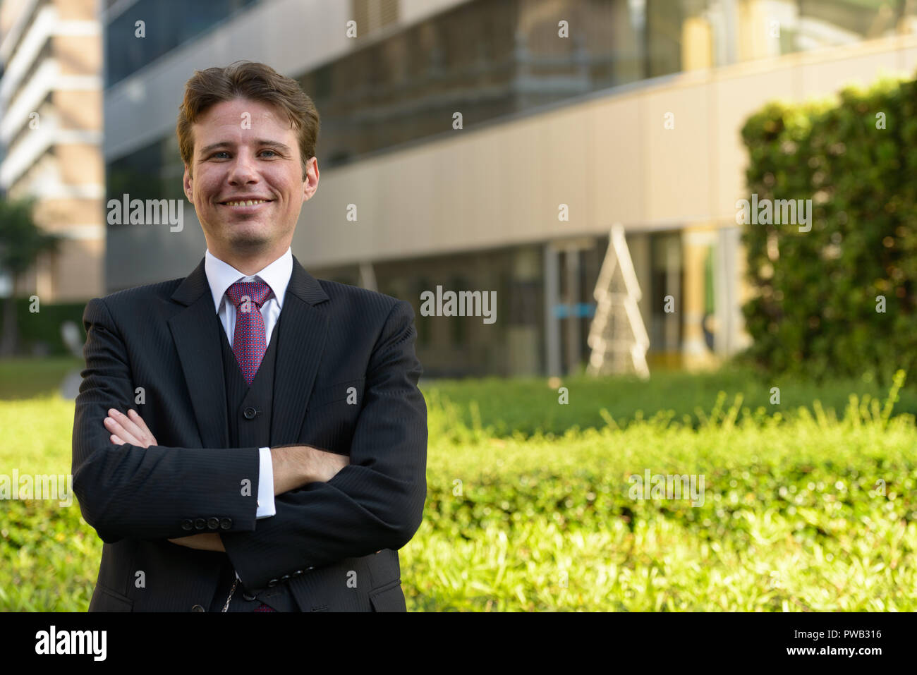 Happy businessman smiling with arms crossed in front of modern g Stock ...