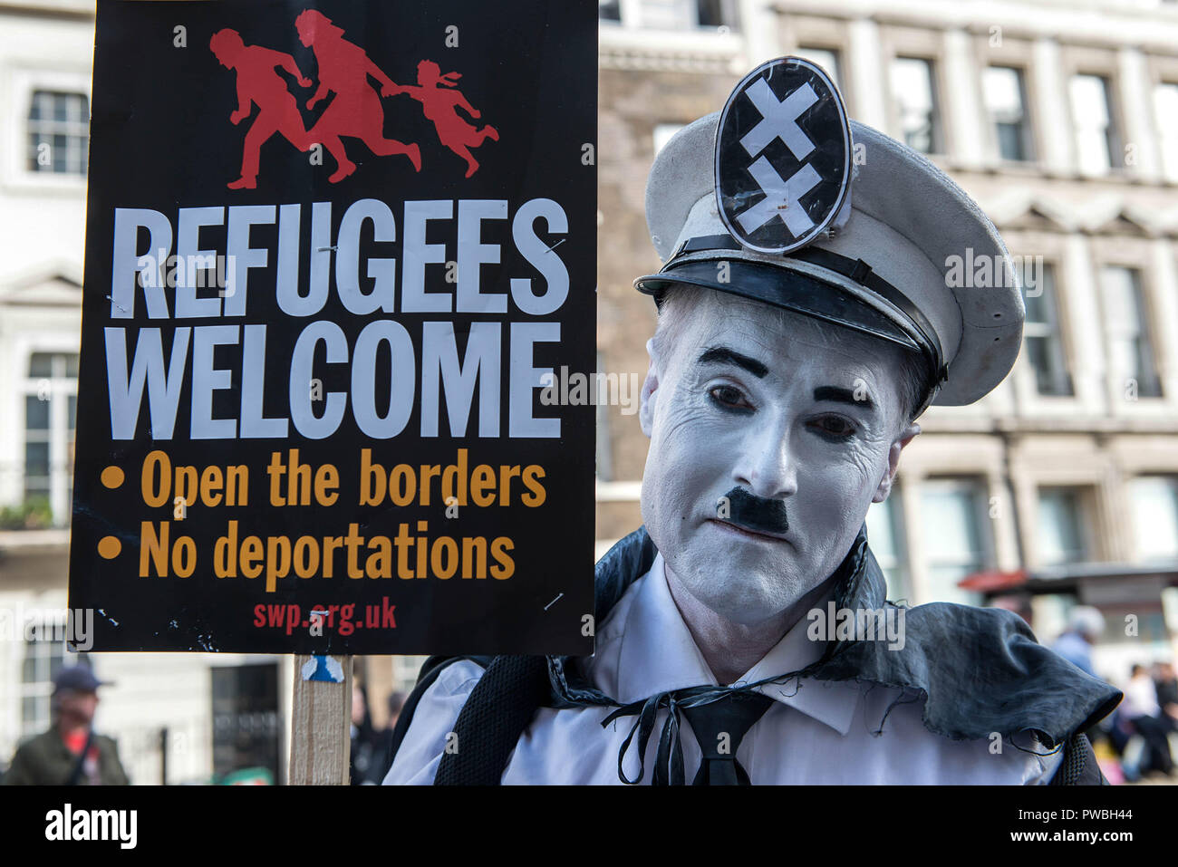 Protester seen wearing make-up to looks like Hitler and holding an antiracism banner at the antifascist demonstration against the DFLA in London. Counter demonstration organised by United Against Racism & Islamophobia, Trade Unions and Stand Up to Racism marched from Old Palace Yard to Whitehall in an attempt to block the route of Democratic Football Lads Alliance (DFLA) march in London. During the counter demonstration there were incidents where DFLA supporters attempted to get close to the anti-racist protesters, that were controlled by the police. Stock Photo