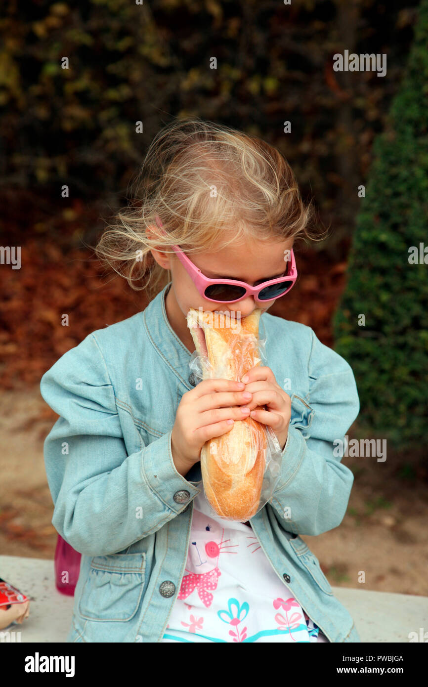 Little girl eating a baguette in the grounds of the Palace of Versailles Stock Photo