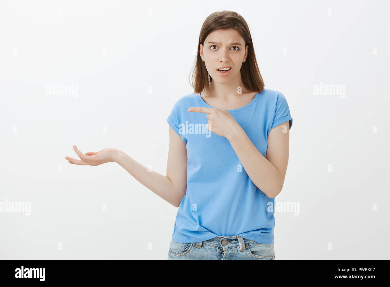 You really talking about this crap. Unimpressed snobbish woman in casual outfit, pointing left with forefinger and raising palm in clueless gesture, being uninterested and disappointed over grey wall Stock Photo