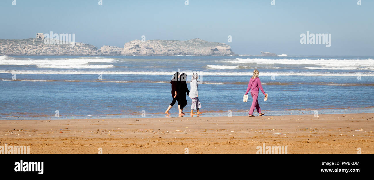 Morocco Essaouira a group of four young local women wearing headscarves walk barefoot on the beach Stock Photo