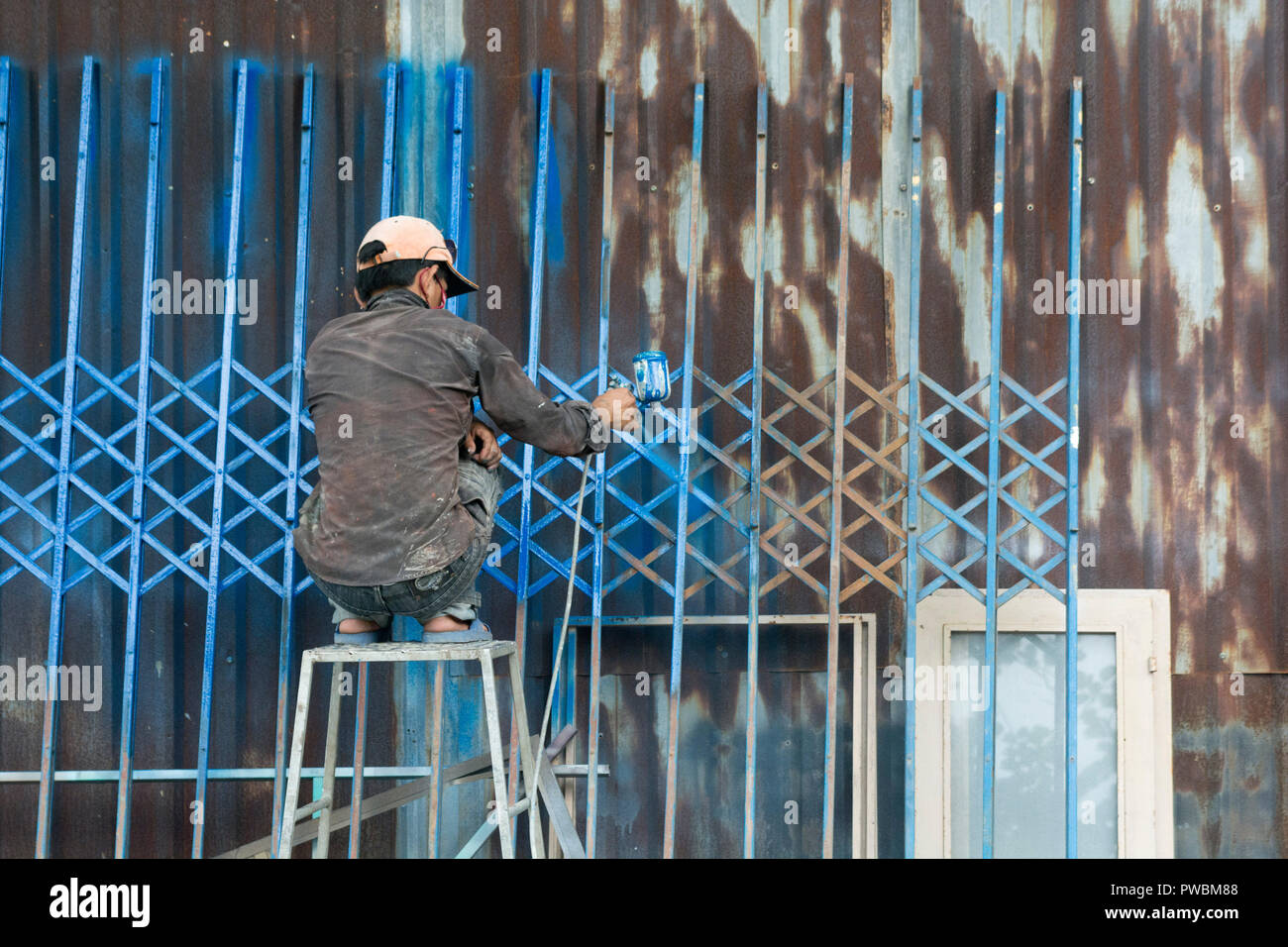 Vietnamese worker painting a fence in Blue, Hoi An, Vietnam Stock Photo