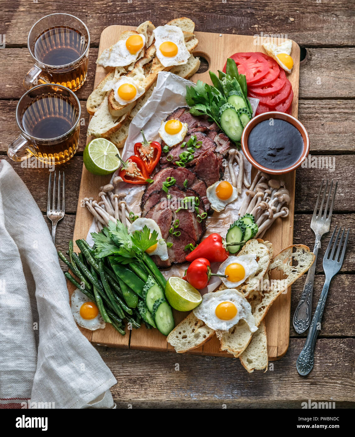 Breakfast meals variety flat lay. Top view on buffet wooden board with meat, eggs, vegetables, bread etc Stock Photo