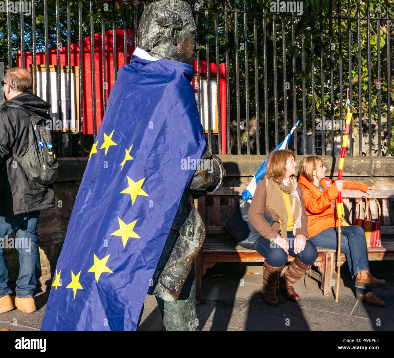 Poet Robert Fergusson statue draped in EU stars flag with women sitting on bench after AUOB march, Canongate, Royal Mile, Edinburgh, Scotland, UK Stock Photo