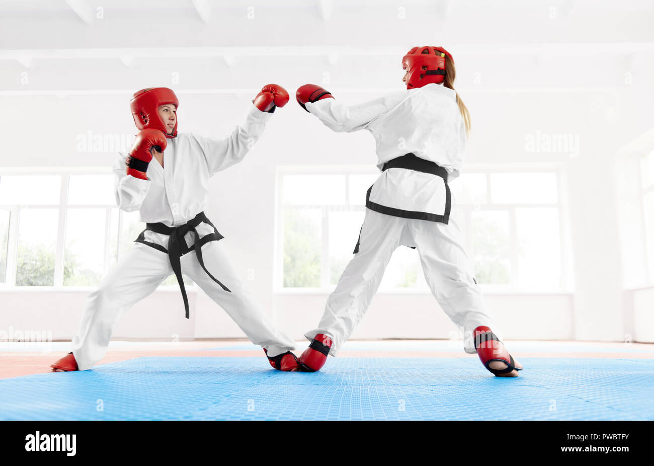 Two professional female fighting, using karate technique kick and punch at bright class. Fighter wearing in special red protective gloves and helmet with special shoes for fight boxing together. Stock Photo