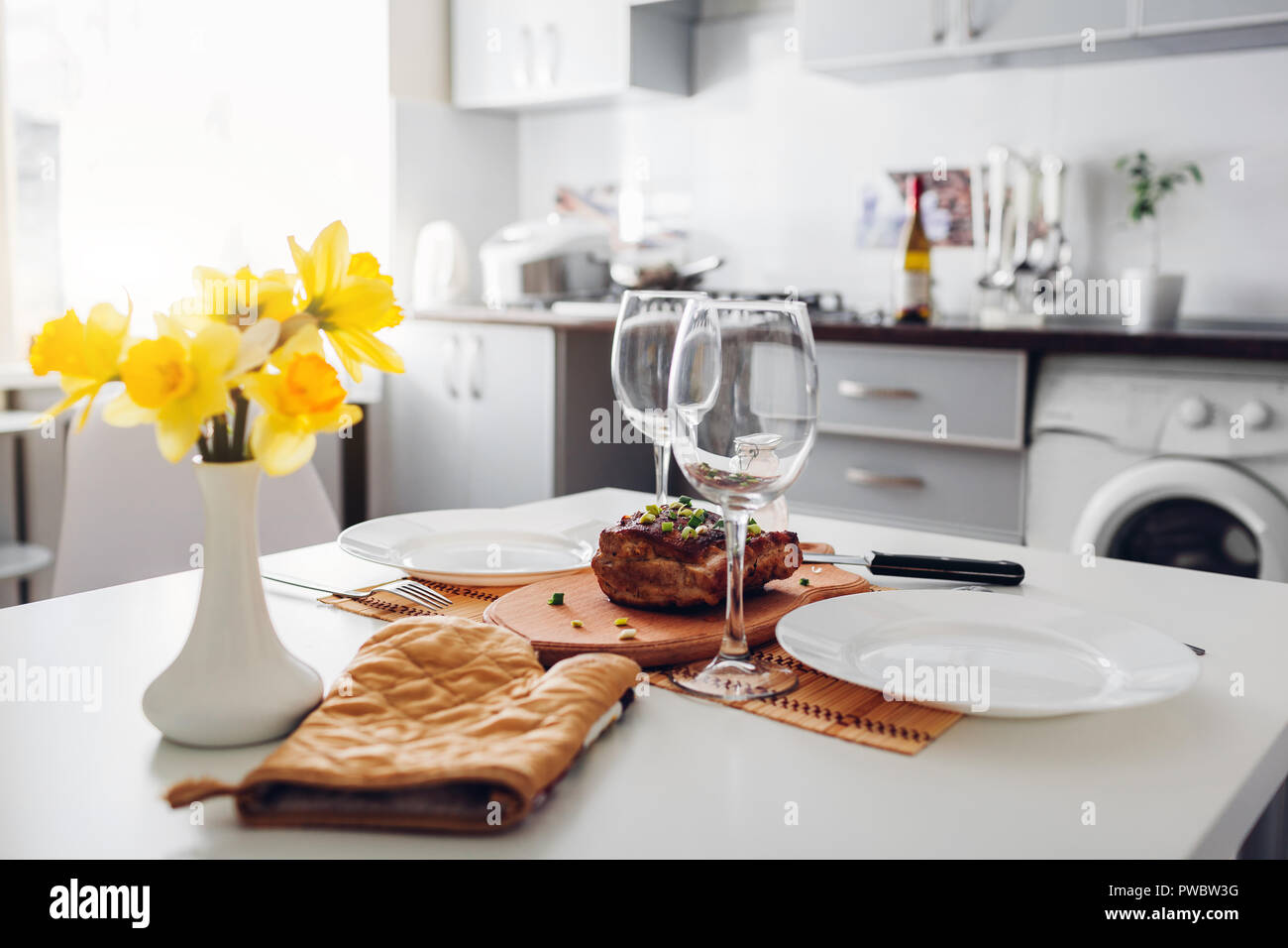 Dinner for two served in kitchen. Modern kitchen design. Roasted meat. Clean kitchen decorated with flowers Stock Photo