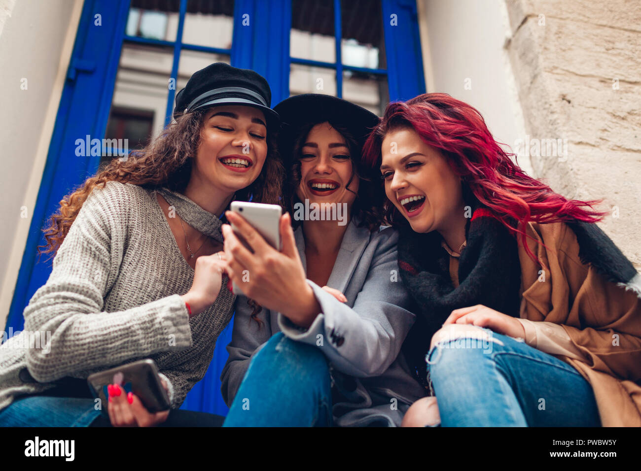 Outdoor shot of three young women looking at smartphone and laughing by ...