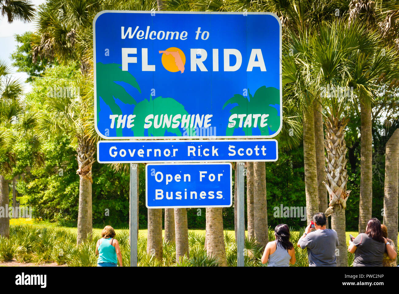 Tourists pull over to take photo with bright blue 'Welcome to Florida' the sunshine state sign at state borderline with Palm trees in Florida Line Stock Photo