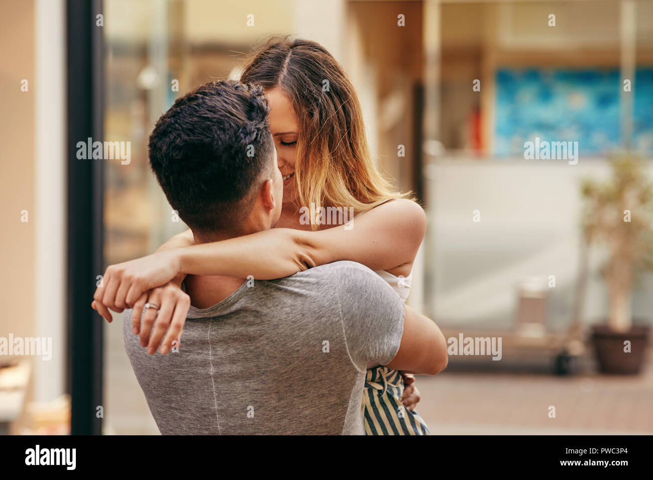Affectionate young couple embracing and sharing a romantic kiss while standing together on a street in the city Stock Photo