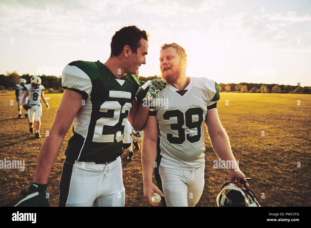 Two smiling American football players talking together while walking off a field after practice on a sunny afternoon Stock Photo