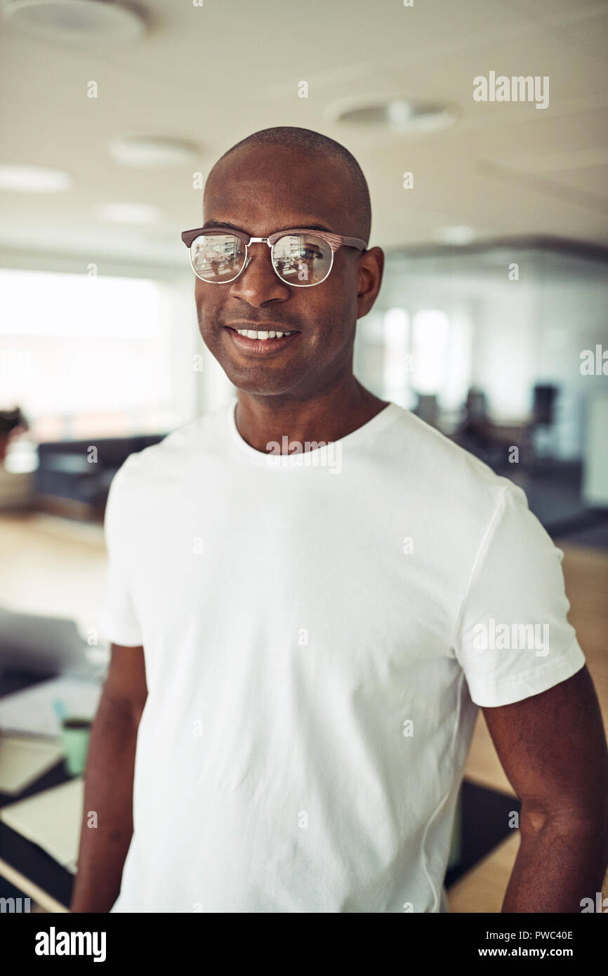 Casually dressed African businessman wearing glasses and smiling while standing alone in a modern office Stock Photo